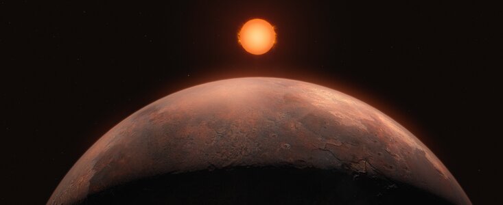 The image is an artist’s impression of an exoplanet. A rusty planet looms in the forefront, half of its sphere taking up most of the frame. The top of the planet is brown and red, illuminated by a small star shining in the distance. The lower part of the sphere is shrouded in darkness. The star is aligned with the planet, in the middle of the image. Compared to the giant planet, the star looks small. In the black background are some very tiny stars.