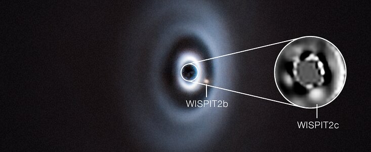 A telescopic image of a flat, inclined fuzzy disc with bright rings and dark gaps, all concentric. There is a small blob in one of those gaps. An inset that zooms in on the centre of the disc shows a second blob in another gap.