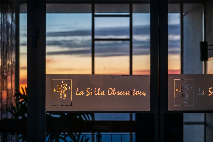 This landscape image shows a sign on glass that shows the ESO logo followed by “La Silla Observatory
