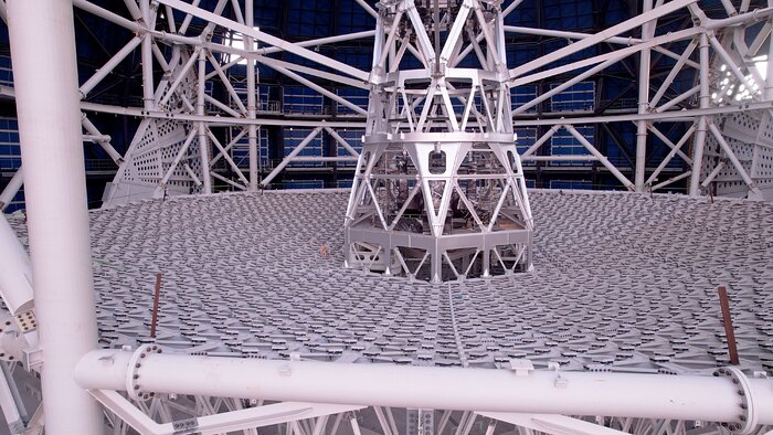 Along the left hand side and bottom of the image are larger white support beams which hold a net-like white structure. In the background are more white support beams and in the middle is a tower that attaches to the outside support beams.