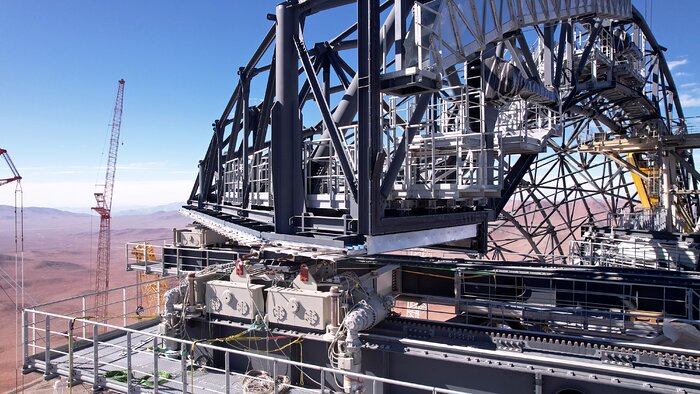 In the centre of the image are large support beams in an arc, with smaller supports filling it out. There is sawtooth track that spans from the bottom right of the image to the centre with a motor attached to the bottom of the door support structure. Between the beams and on the left of the image is the horizon and the red desert.