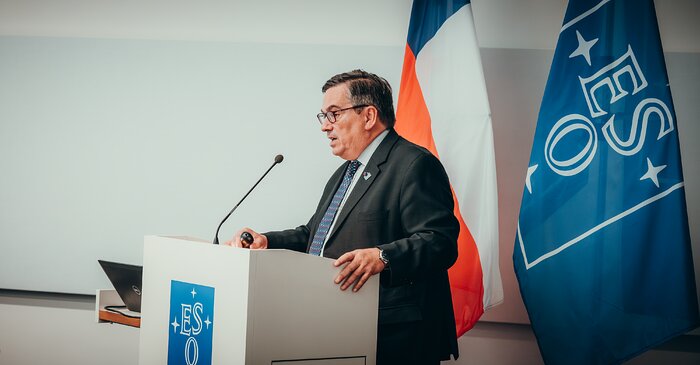 Xavier Barcons, ESO's Director Manager as of 2024, stands in front of a white podium with ESO's logo while delivering a speech. Behind him stands the ESO's flag with its characteristic pale blue background and white rectangle with the letters 