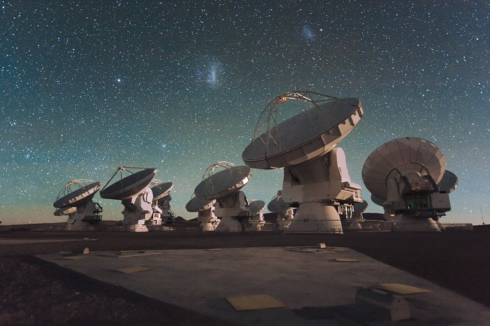 El Atacama Large Millimeter/submillimeter Array (ALMA) de noche, debajo de las nubes Magallanes