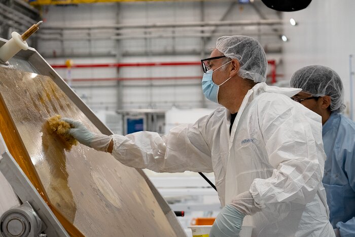 A person wearing a hair net, face mask, scrubs and gloves moves a sponge over an amber-coloured, hexagonal surface being held in place by a metal structure.