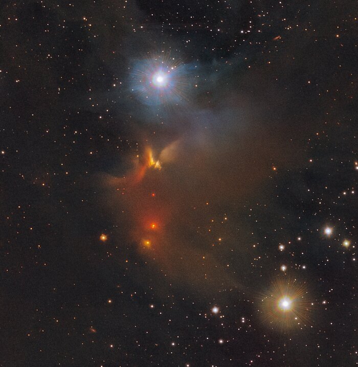 This image shows stars and clouds of gas and dust dispersed against a dark background.  A prominent cloud of gas and dust can be seen in the central part of the image.  It is characterized by a red-brown amorphous cloud.  A blue star shines in the upper part, and a yellow star shines brightly in the lower right part of the image.