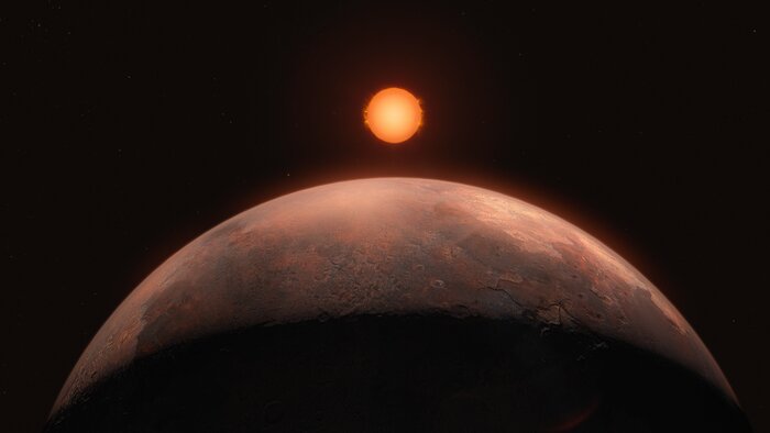 Das Bild ist eine künstlerische Darstellung eines Exoplaneten. Im Vordergrund ragt ein rostfarbener Planet hervor, der mit der Hälfte seiner Oberfläche den größten Teil des Bildes einnimmt. Die Oberseite des Planeten ist braun und rot und wird von einem kleinen Stern in der Ferne beleuchtet. Der untere Teil der Kugel ist in Dunkelheit gehüllt. Der Stern befindet sich in einer Linie mit dem Planeten in der Mitte des Bildes. Im Vergleich zum riesigen Planeten sieht der Stern klein aus. Im schwarzen Hintergrund befinden sich einige sehr kleine Sterne.