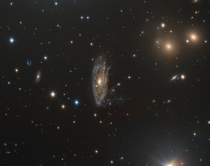 The image shows a colourful backdrop of stars and galaxies against the black cosmos. There’s a large spiral galaxy a the centre of the image. The spiral galaxy appears slightly smudged.