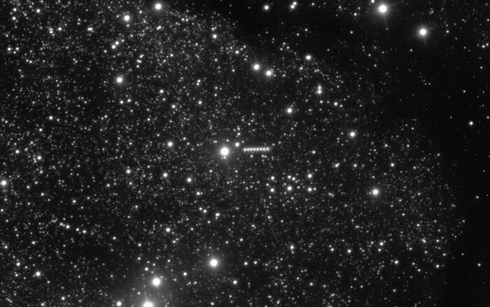 A telescopic image showing many white stars against a black background. At the centre of the image there’s a series of white smudges arranged in a short straight line, with gaps in between, which correspond to a comet that moves from left to right.