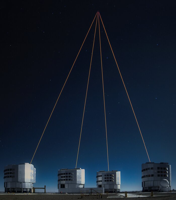 The image shows four massive cylindrical like structures on the bottom. Out of all of these metal structures, a laser is shooting up into the sky to a spot where all four lasers meet.