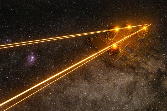 Four yellow laser lines form two sides of a triangle (two lasers for each side), which reaches from the left-hand side of the image to a point in the top right. A closer look at the point of the triangle shows that the lines don’t fully meet but each end in a tiny point. Each line has a glowing spot on it, nearby to the point of the triangle, and together the four yellow spots make a trapezium shape. A diagram showing the location of four telescopes is overlaid here, with one spot inside each telescope. The backdrop is a starry night sky, with large bright grey clouds on the bottom right and two small bright bluish clouds on the left, one inside the laser triangle and the other above it.