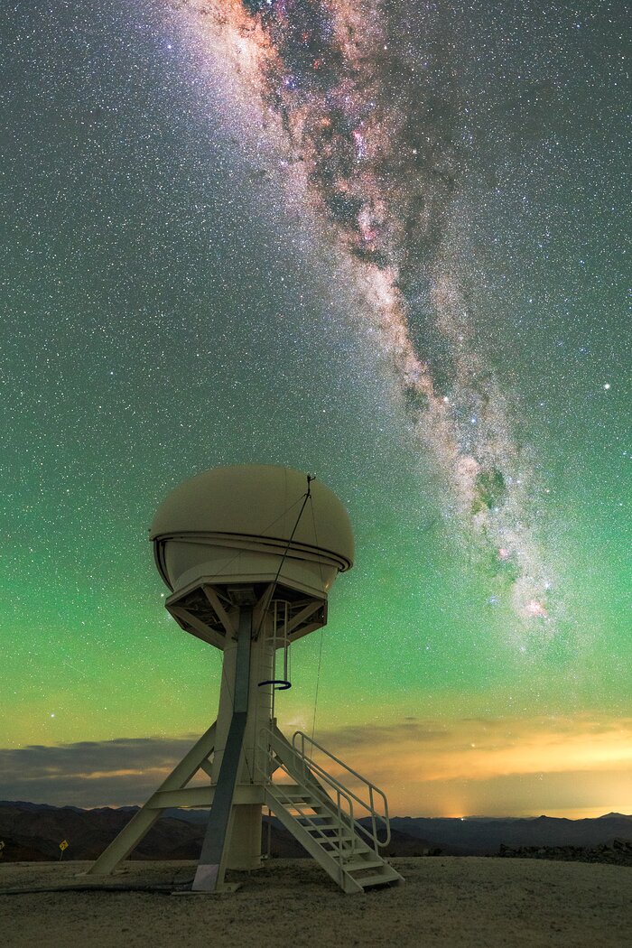 The image shows a strangely shaped telescope in the desert: a spherical dome mounted on a tower supported by several legs. Above the telescope, the Milky Way is visible in the starry sky.